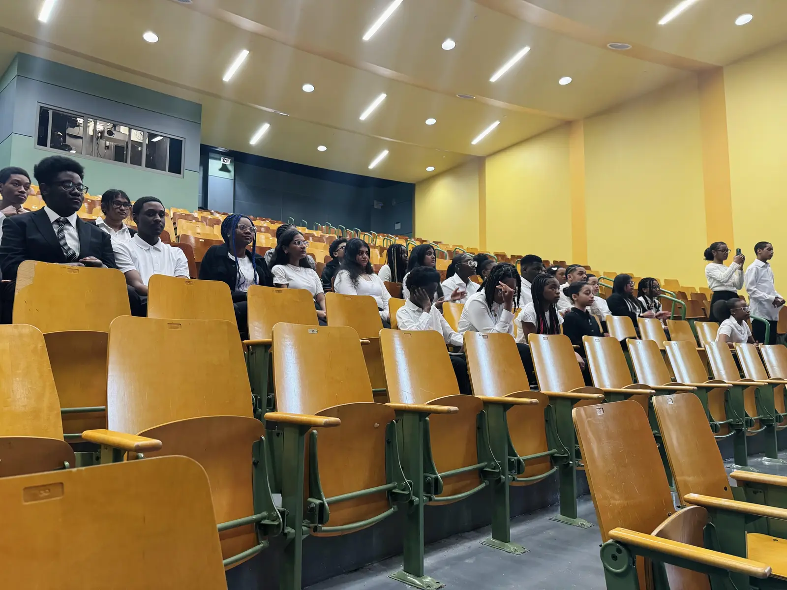 Students in uniform seated in an auditorium during a school assembly