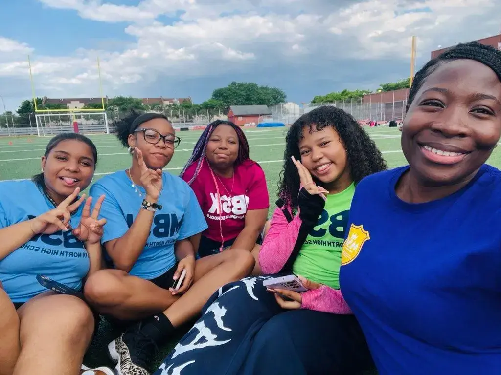 Five students smiling together on a school athletic field
