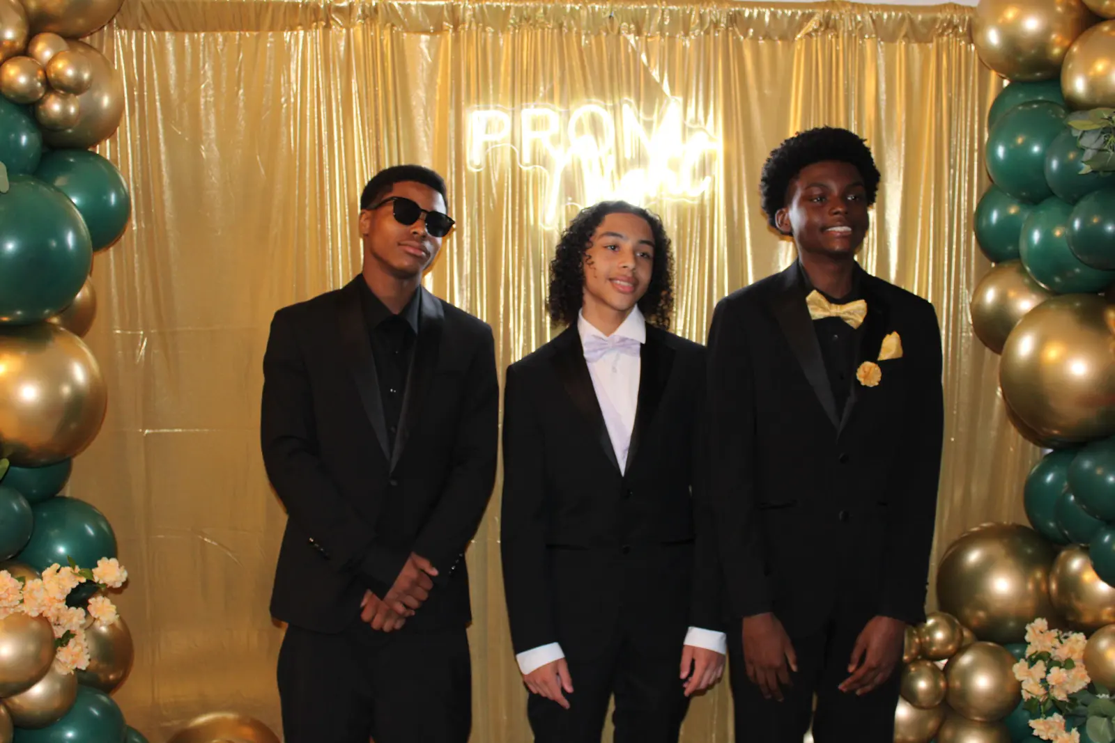 Three male students in formal suits posing at prom photo backdrop