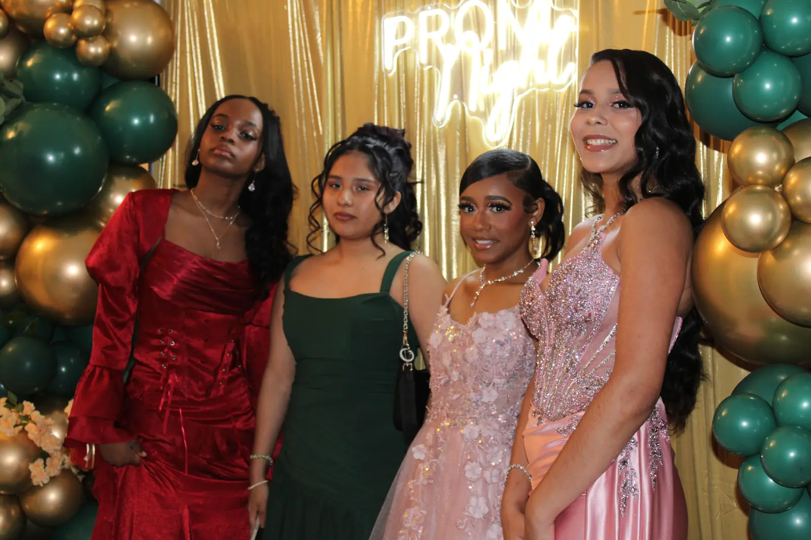 Four students posing together in formal gowns at prom night