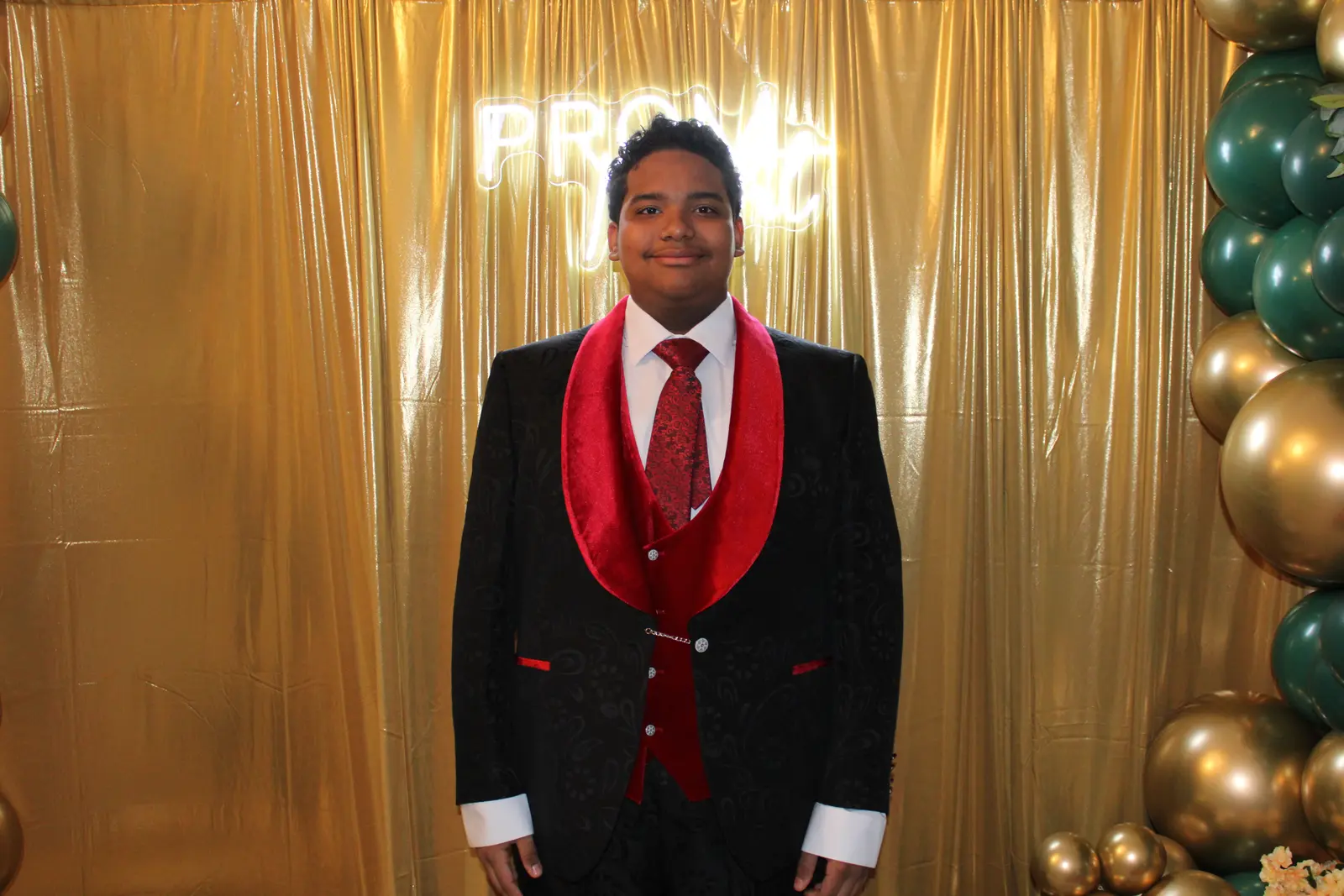 Student in black and red tuxedo posing at prom photo backdrop