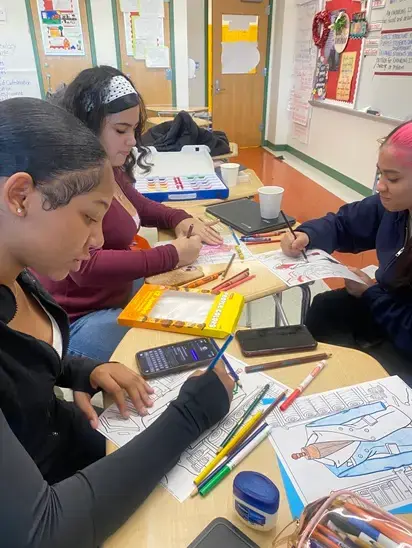 Three students coloring together at classroom desks