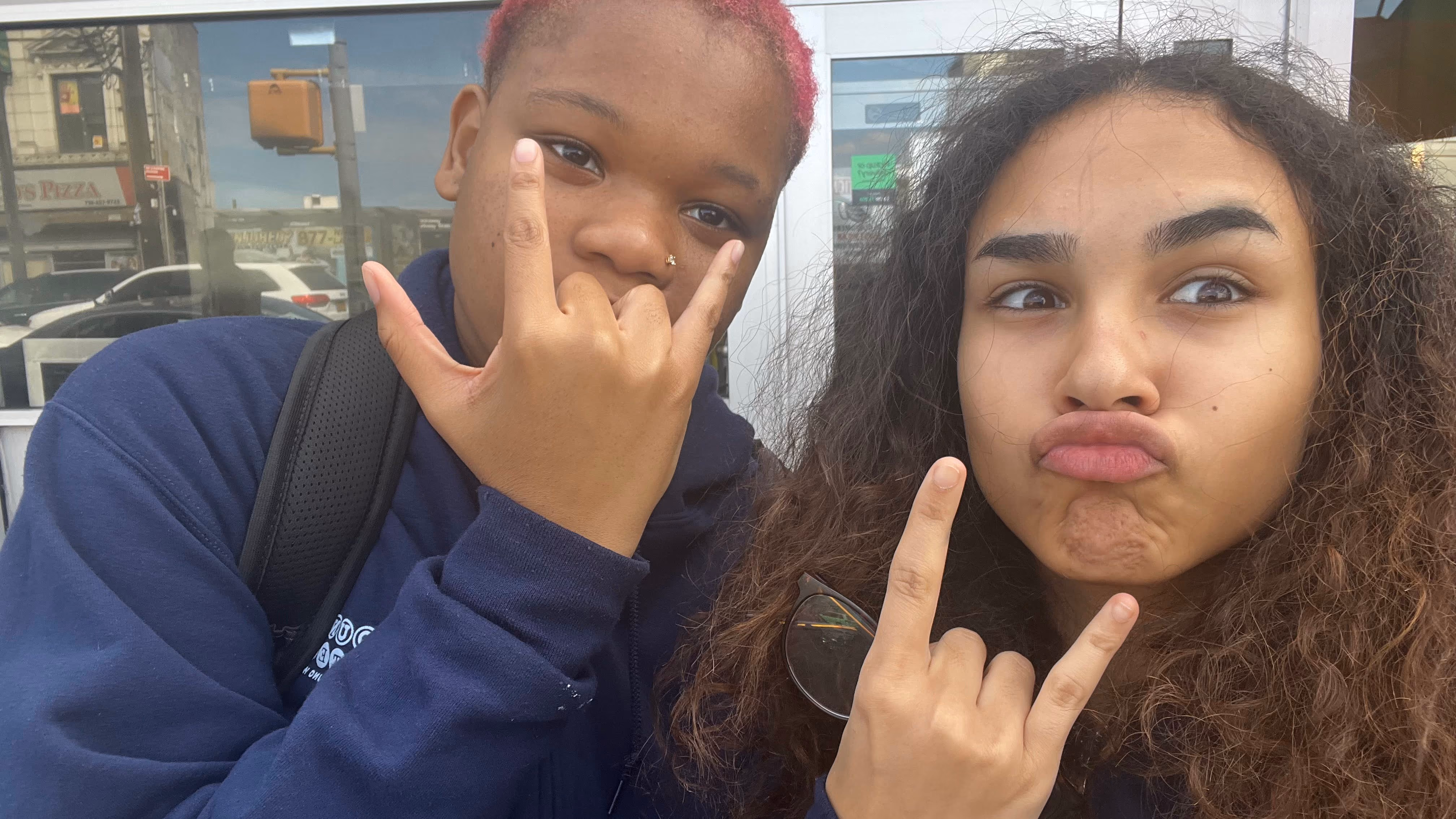 Two students making hand gestures and silly faces outside