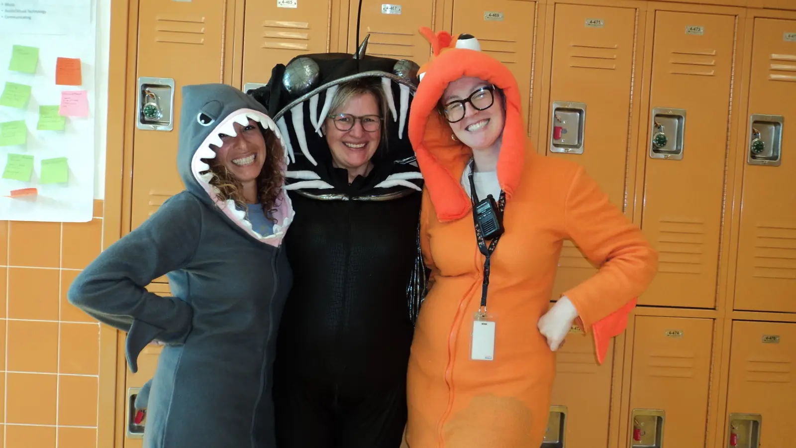 Three staff members in fish and shark costumes by school lockers