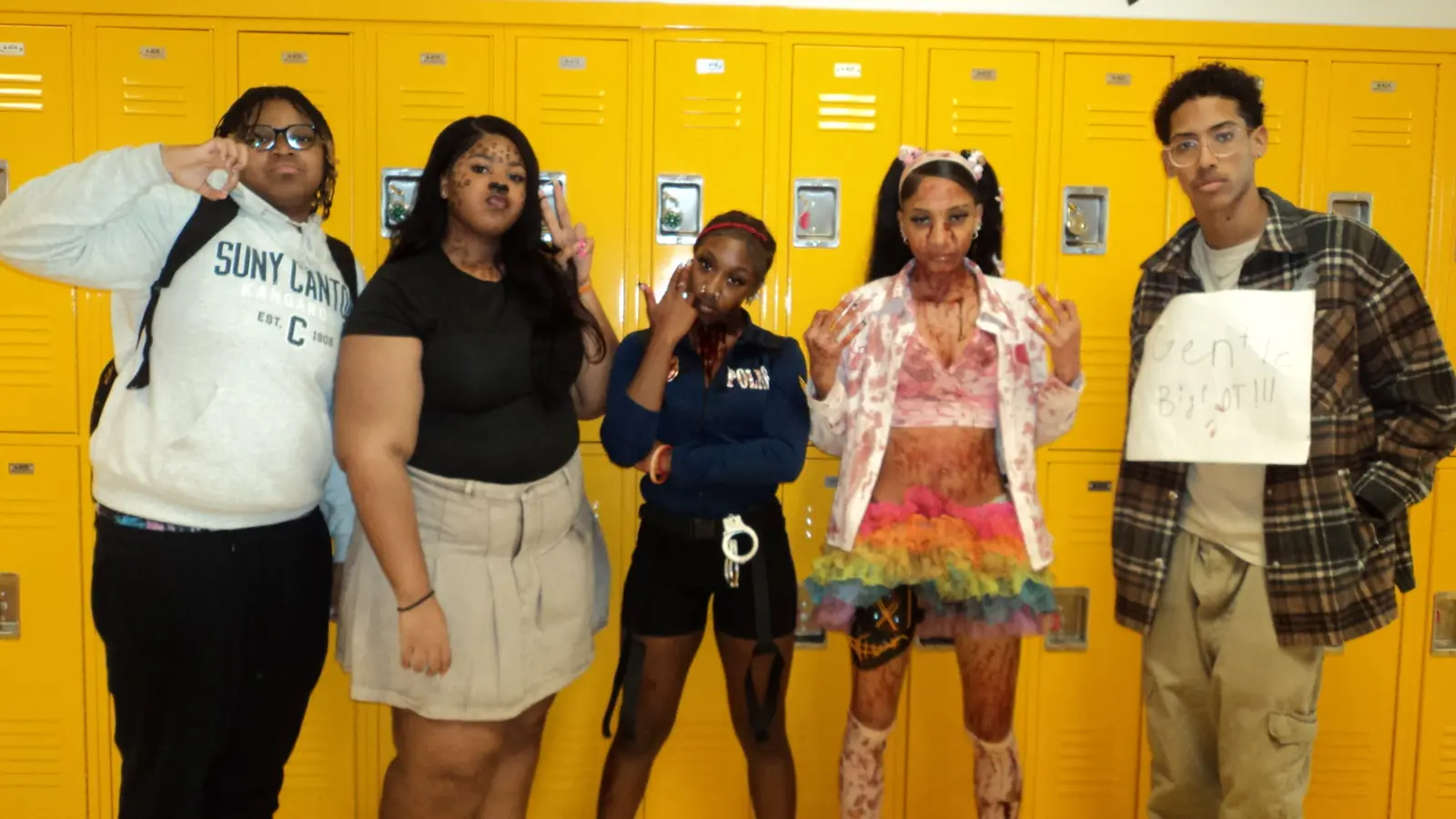Five students in Halloween costumes posing by yellow school lockers