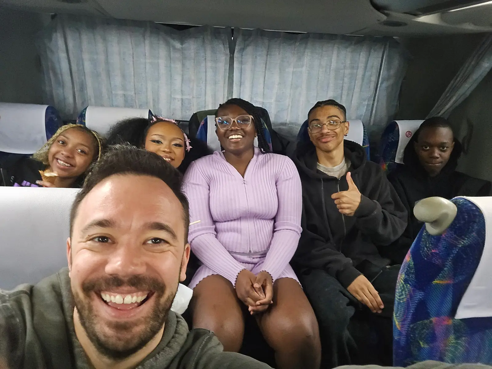 Teacher and students smiling together on a school field trip bus