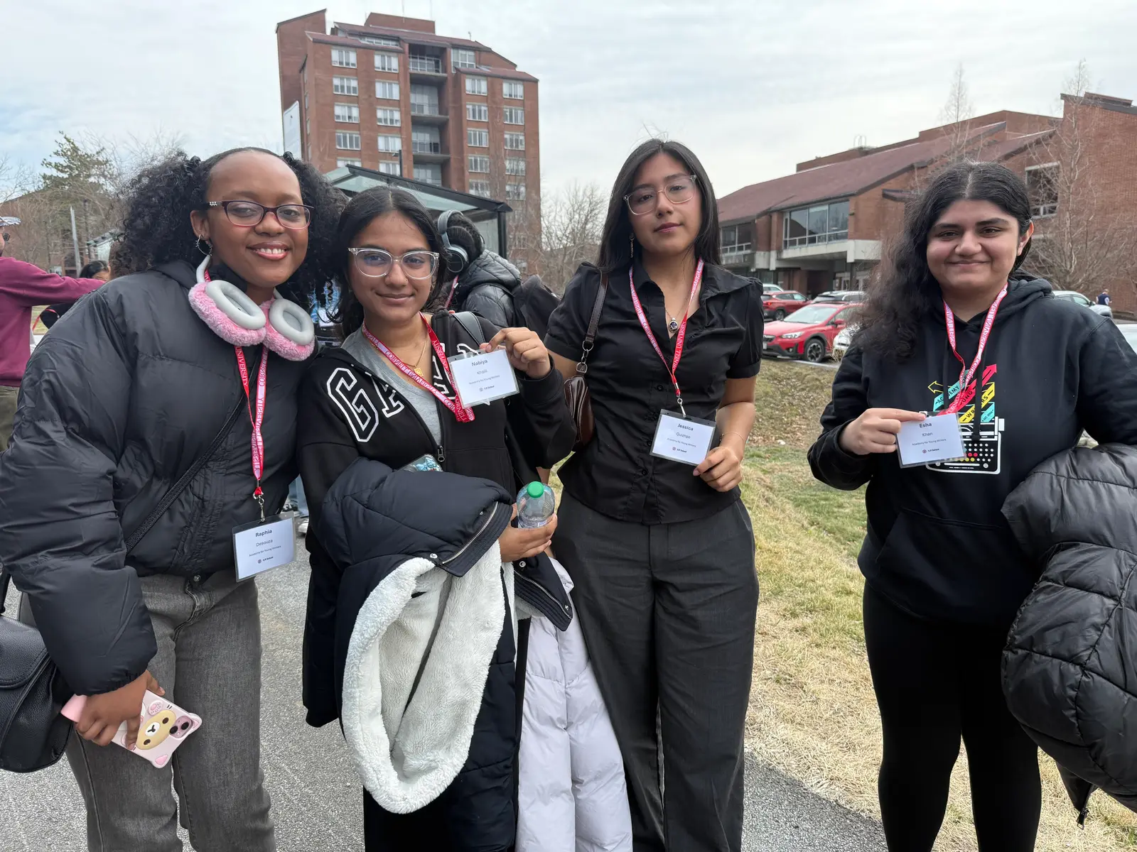 Four students wearing lanyards pose together at an outdoor event