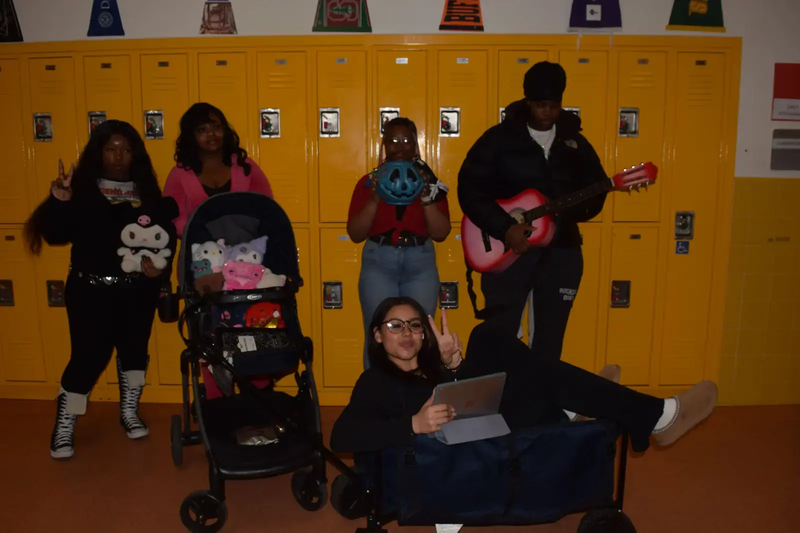 Five students posing together in front of yellow school lockers