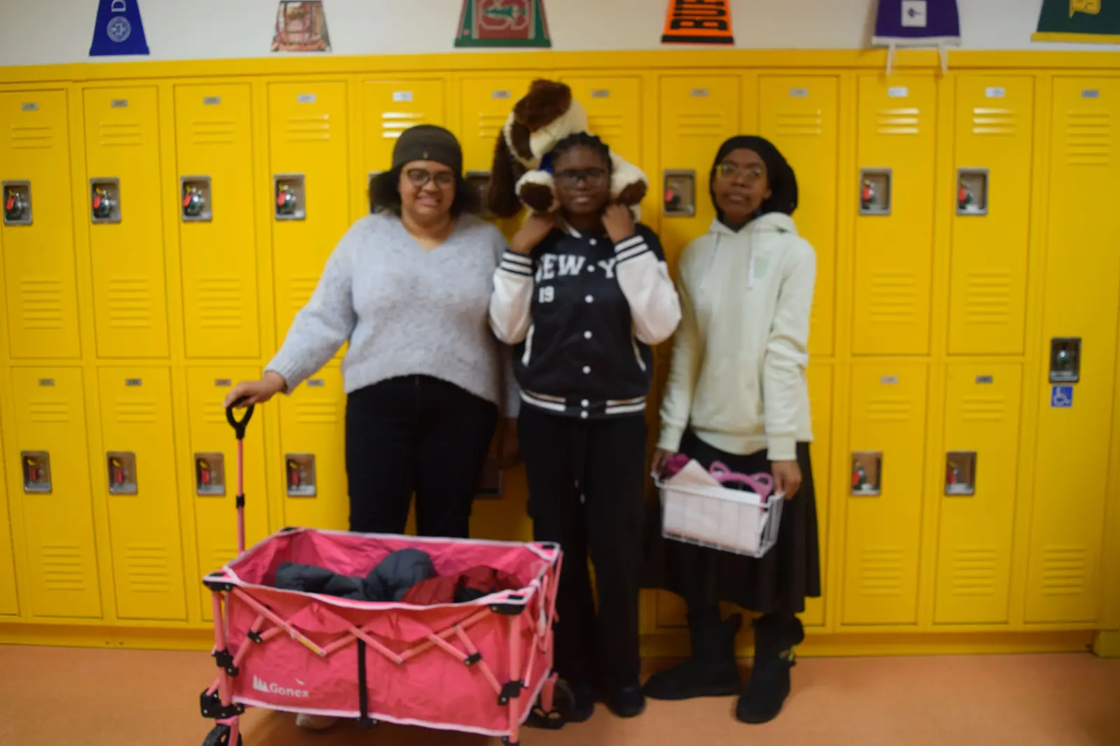 Three students posing together by yellow school lockers with wagon