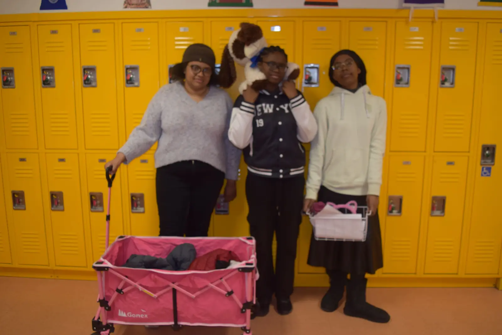 Three students posing in school hallway with yellow lockers