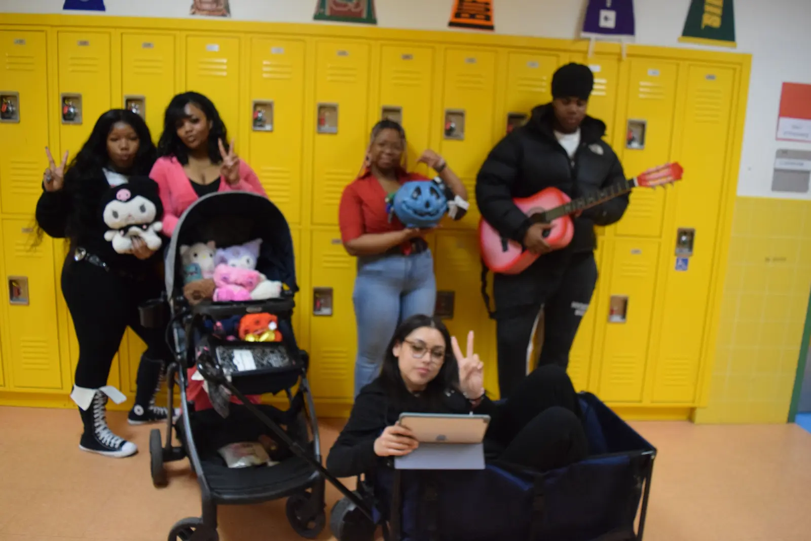 Students posing in school hallway with guitar stuffed animals and stroller