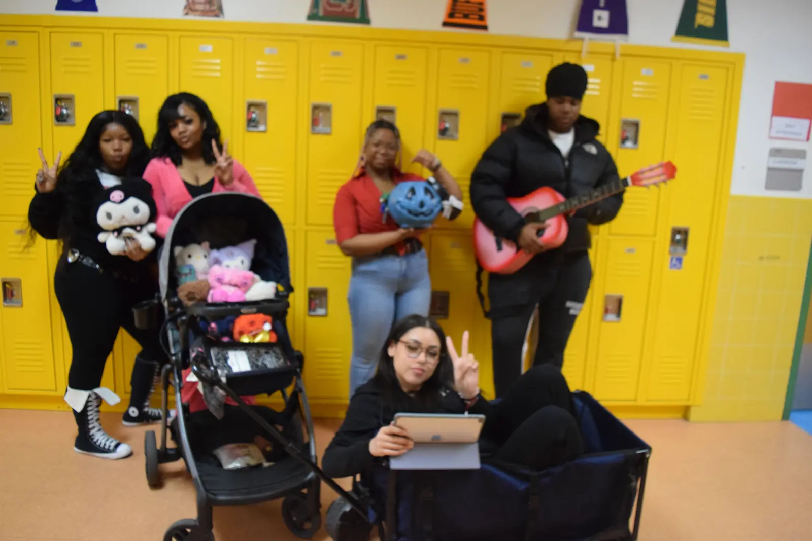 Students posing with guitar stuffed animals and tablet by school lockers
