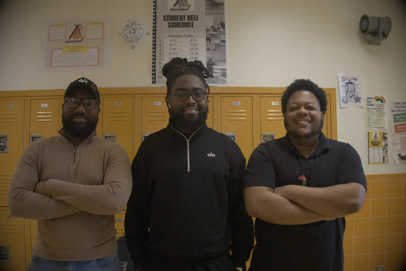 Three smiling staff members standing together in school hallway