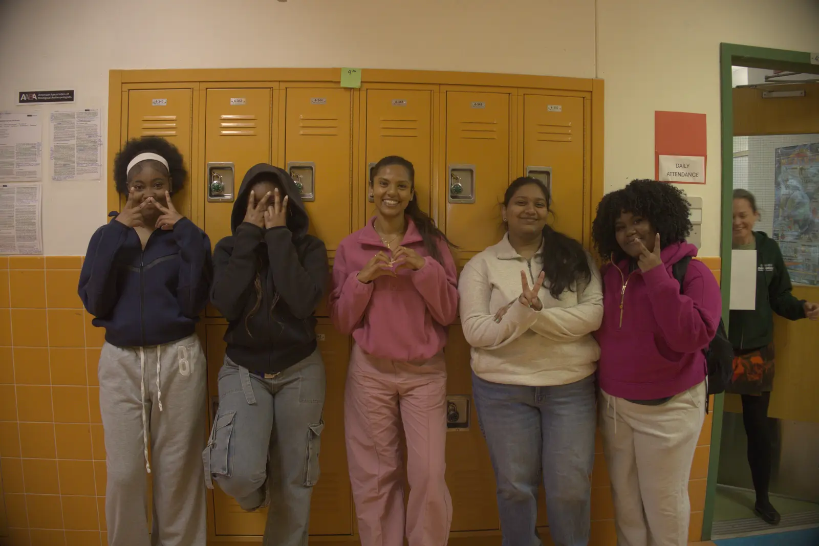 Five students posing together in front of school hallway lockers