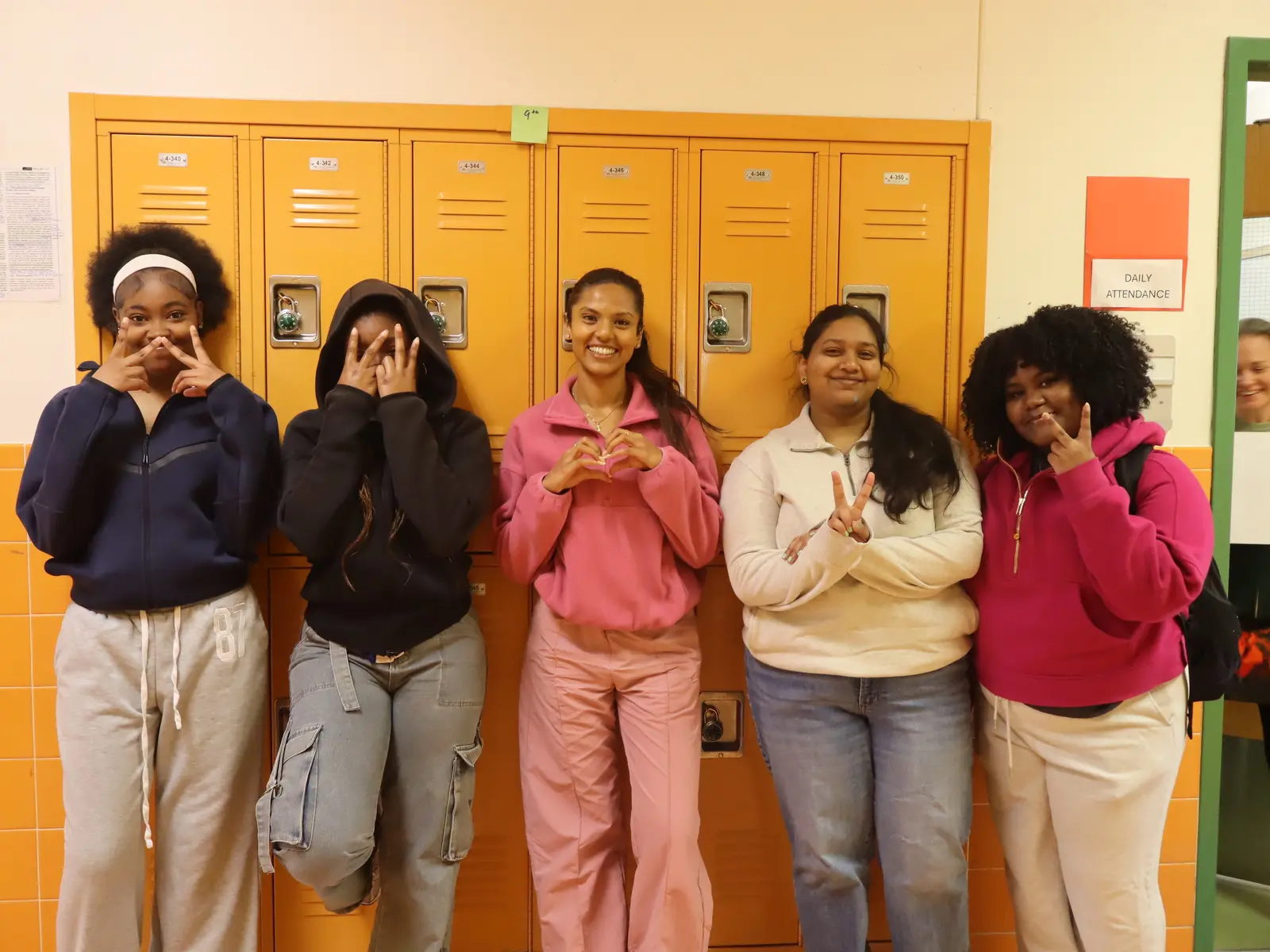 Five students posing and smiling together by school hallway lockers