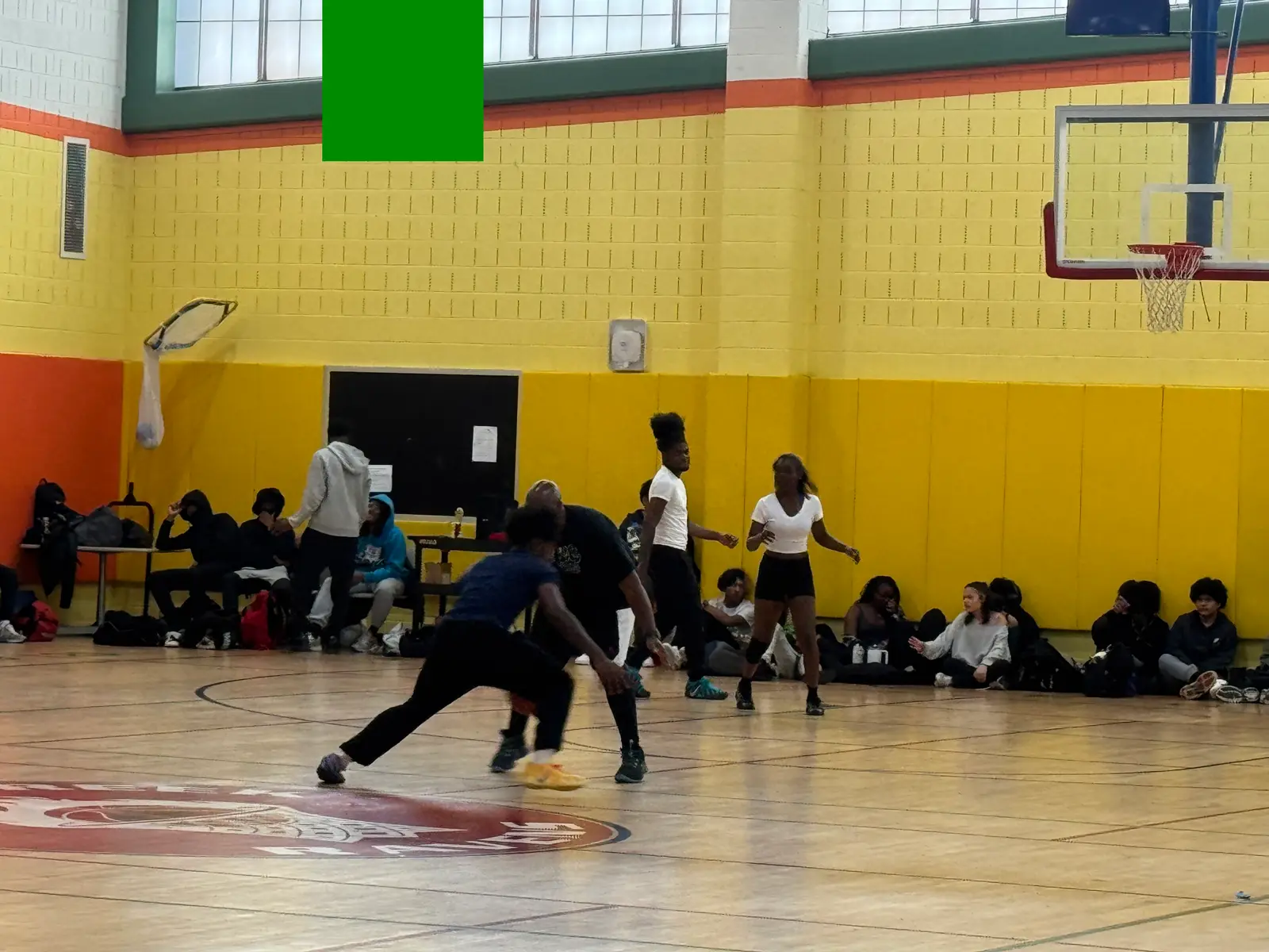 Students playing basketball in a school gymnasium with peers watching