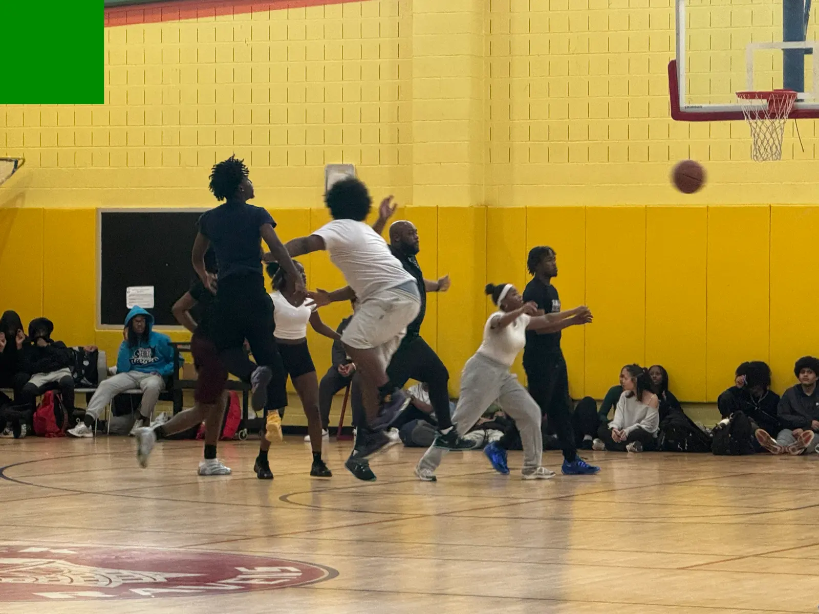 Students playing basketball in a school gymnasium with spectators watching