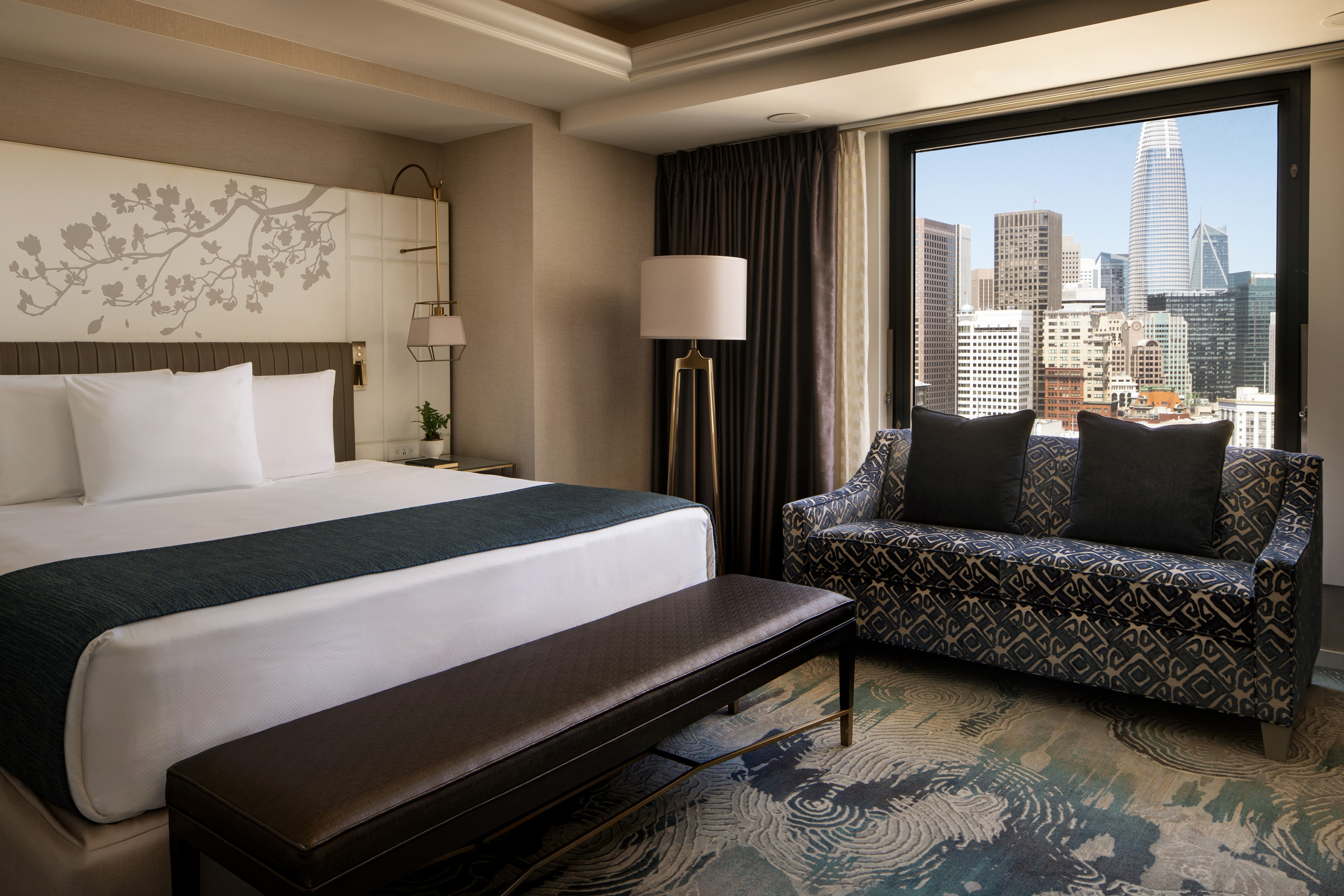 Modern hotel bedroom with sofa and large city-view window.