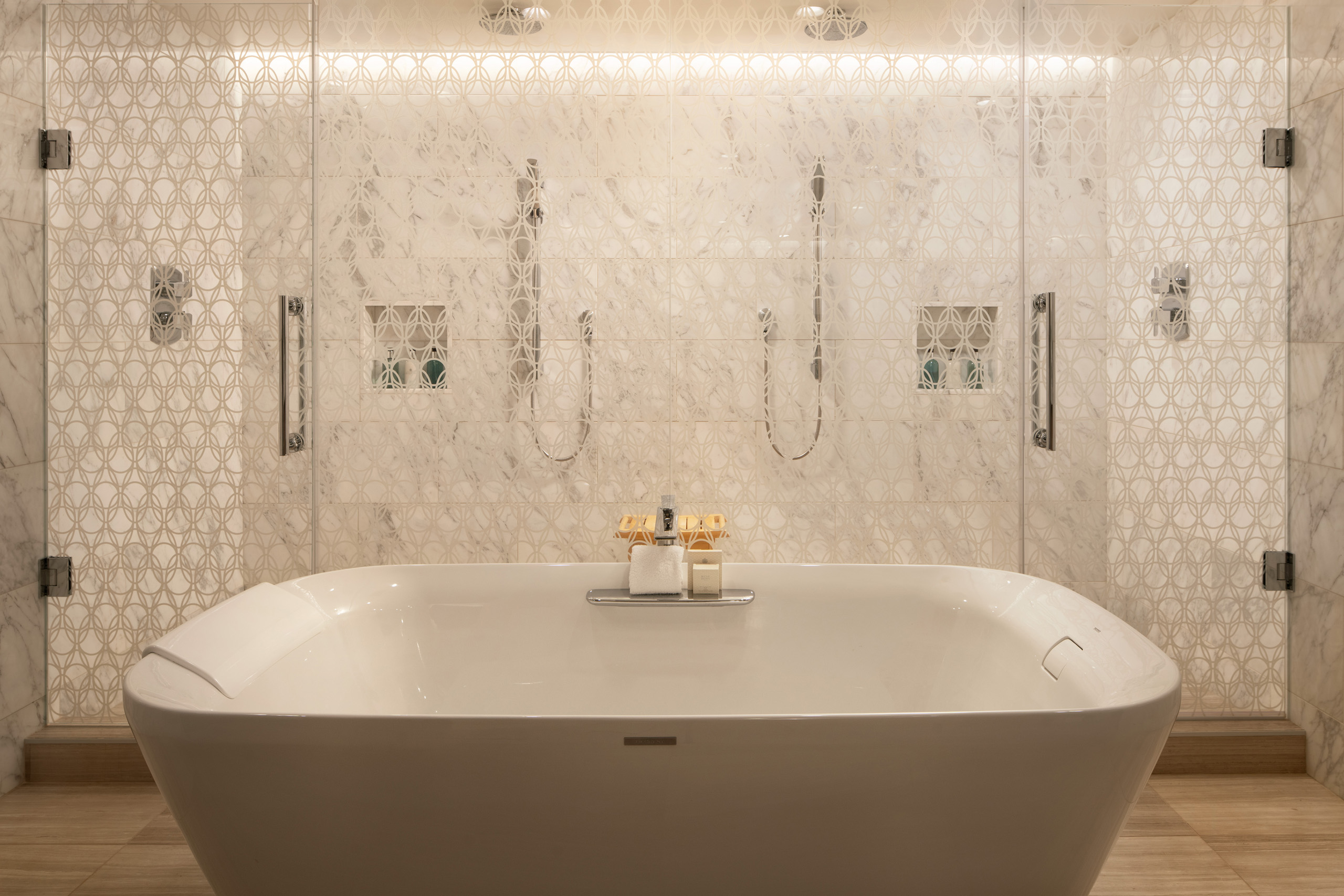 Freestanding soaking tub before glass-enclosed marble shower.