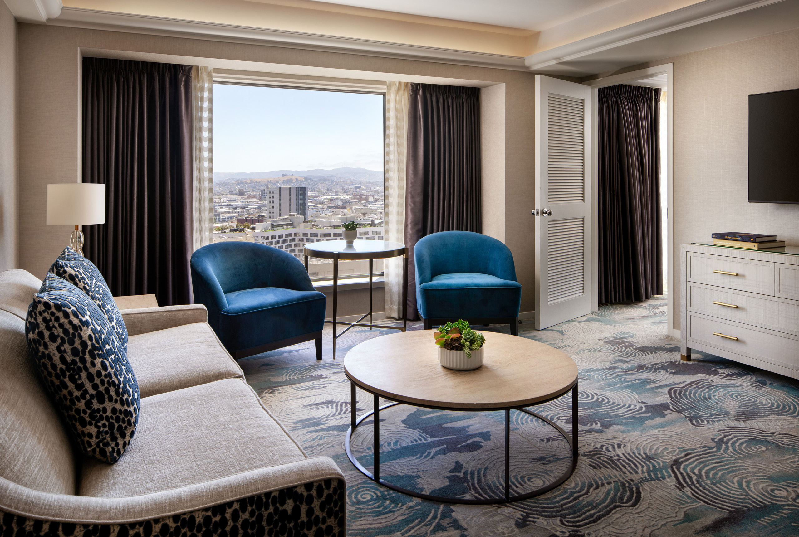 Hotel suite living room with sofa, chairs, coffee table, and city view.