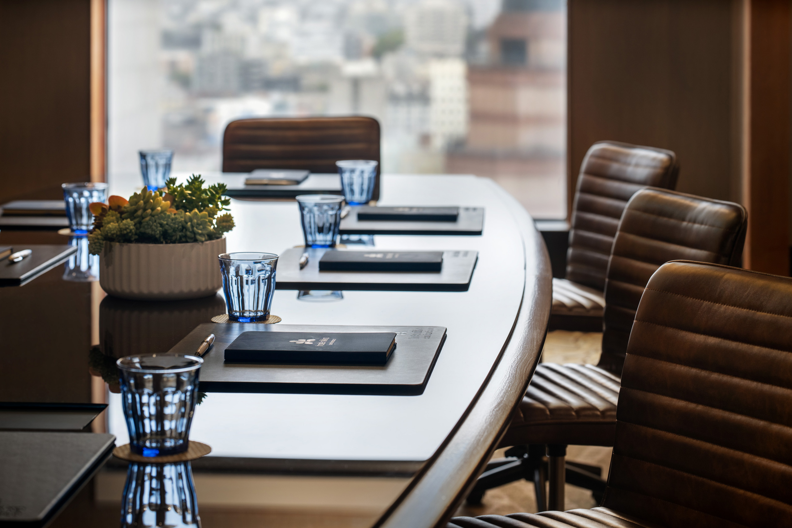 Boardroom table with notebooks, blue glasses, and succulent.