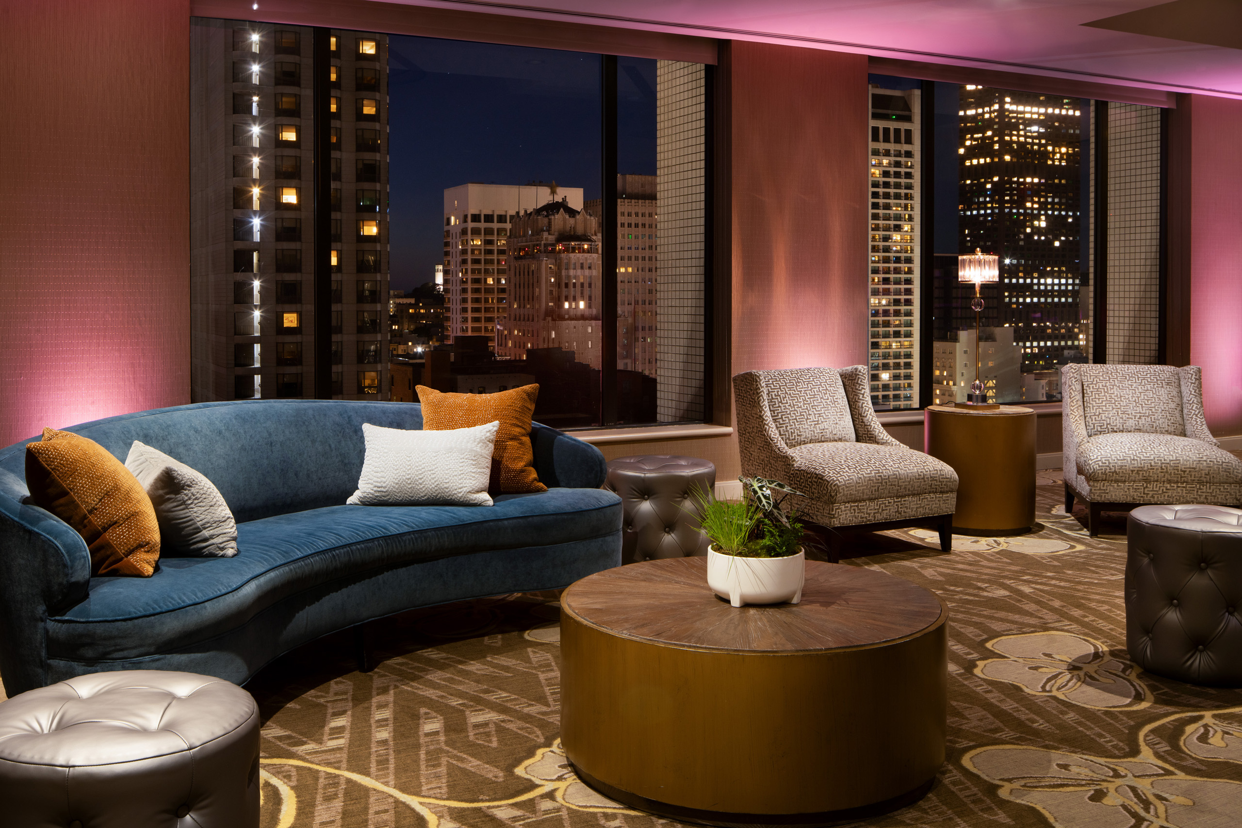Blue velvet sofa and lounge seating overlooking illuminated city skyline.