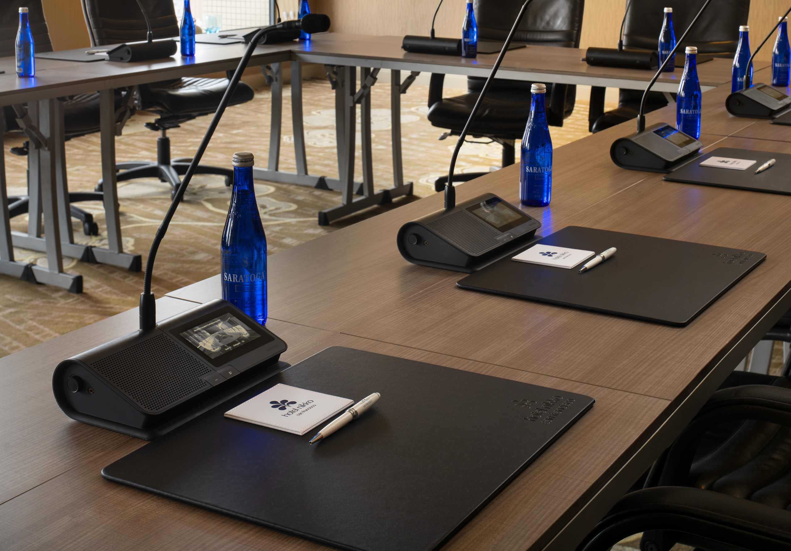 Conference room with microphones, notepads, pens, and bottled water.