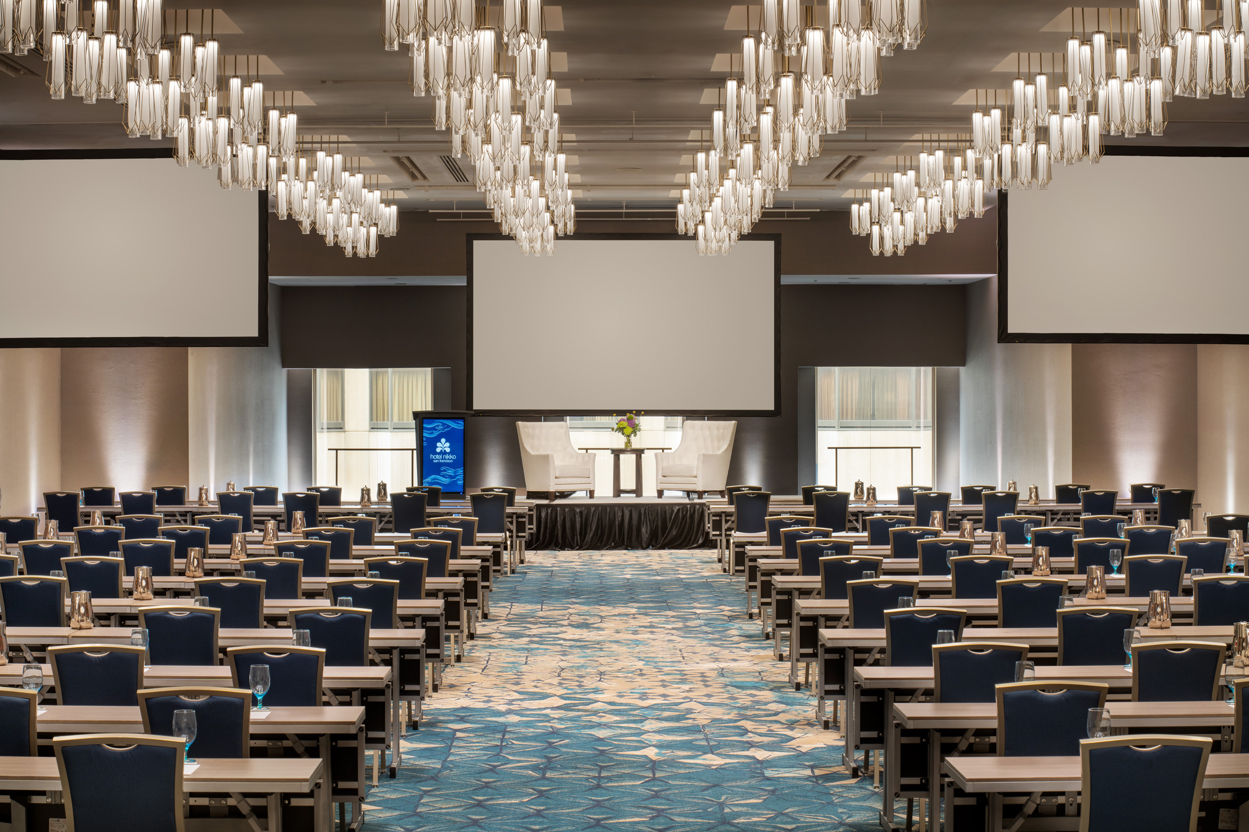 Spacious ballroom classroom setup with stage and presentation screens.