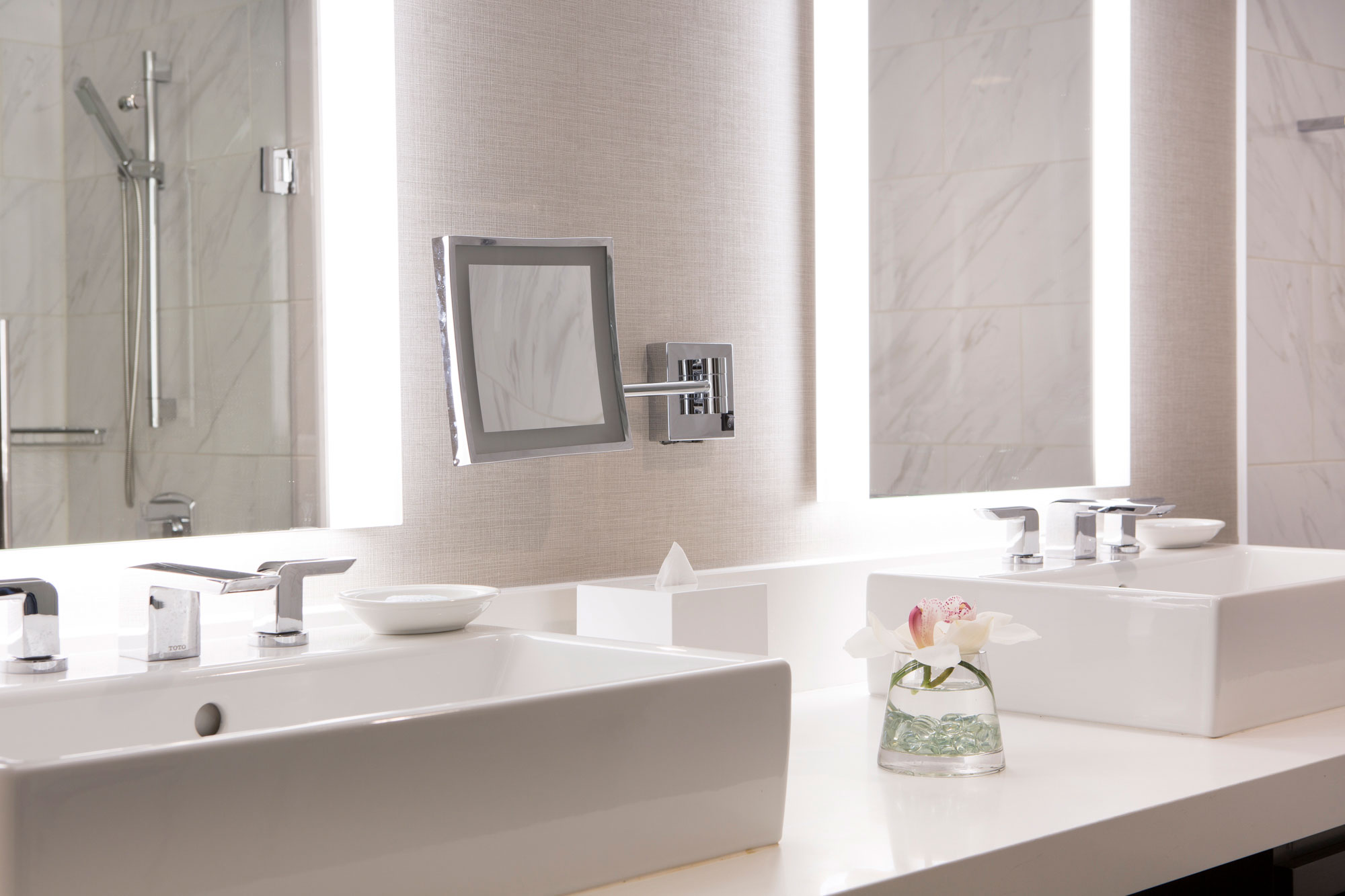 Double vanity in a junior suite bathroom with vessel sinks, illuminated mirrors, chrome fixtures, and marble tile.