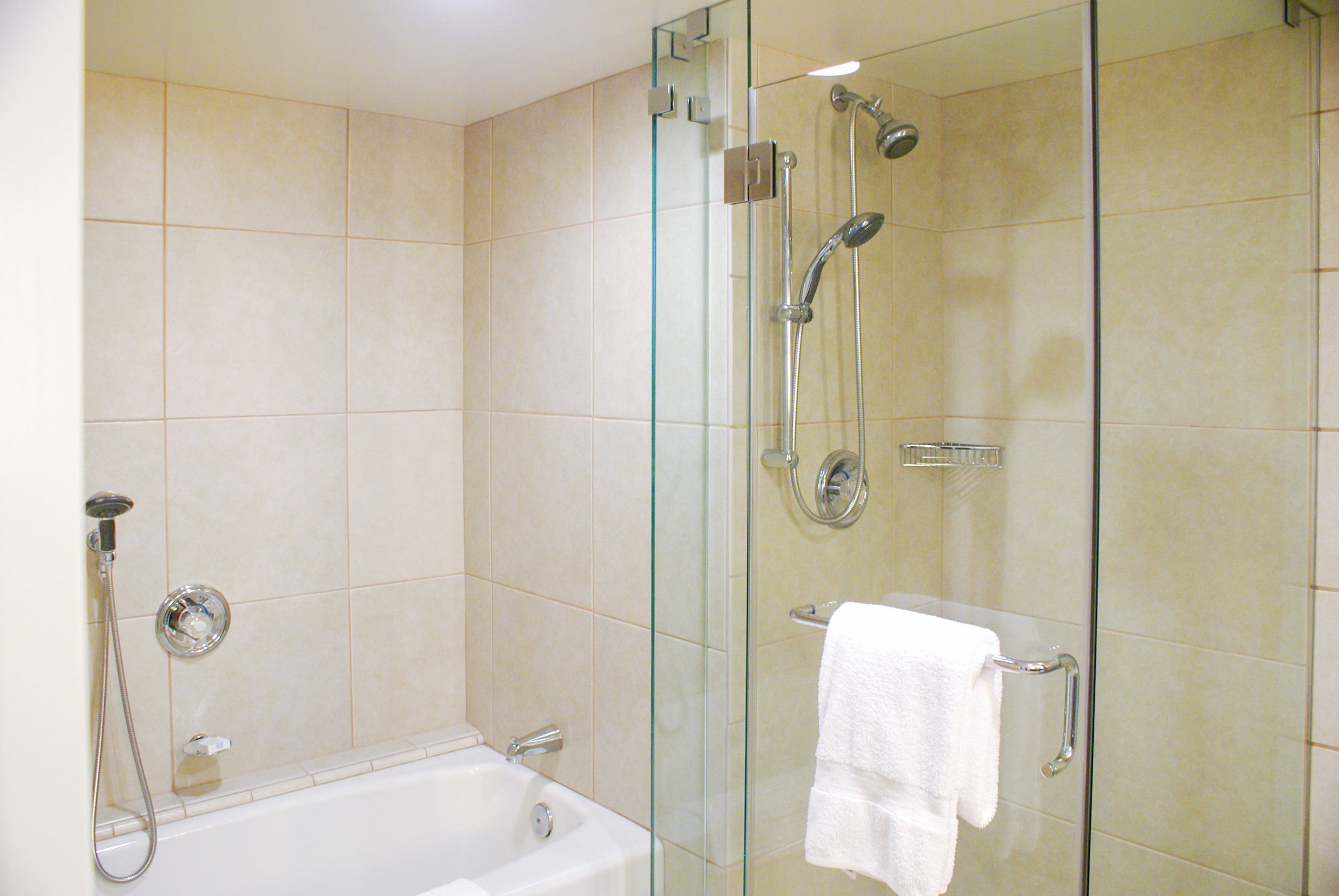 Deluxe hotel bathroom with a soaking tub, glass-enclosed shower, beige tile, chrome fixtures, and white towels.