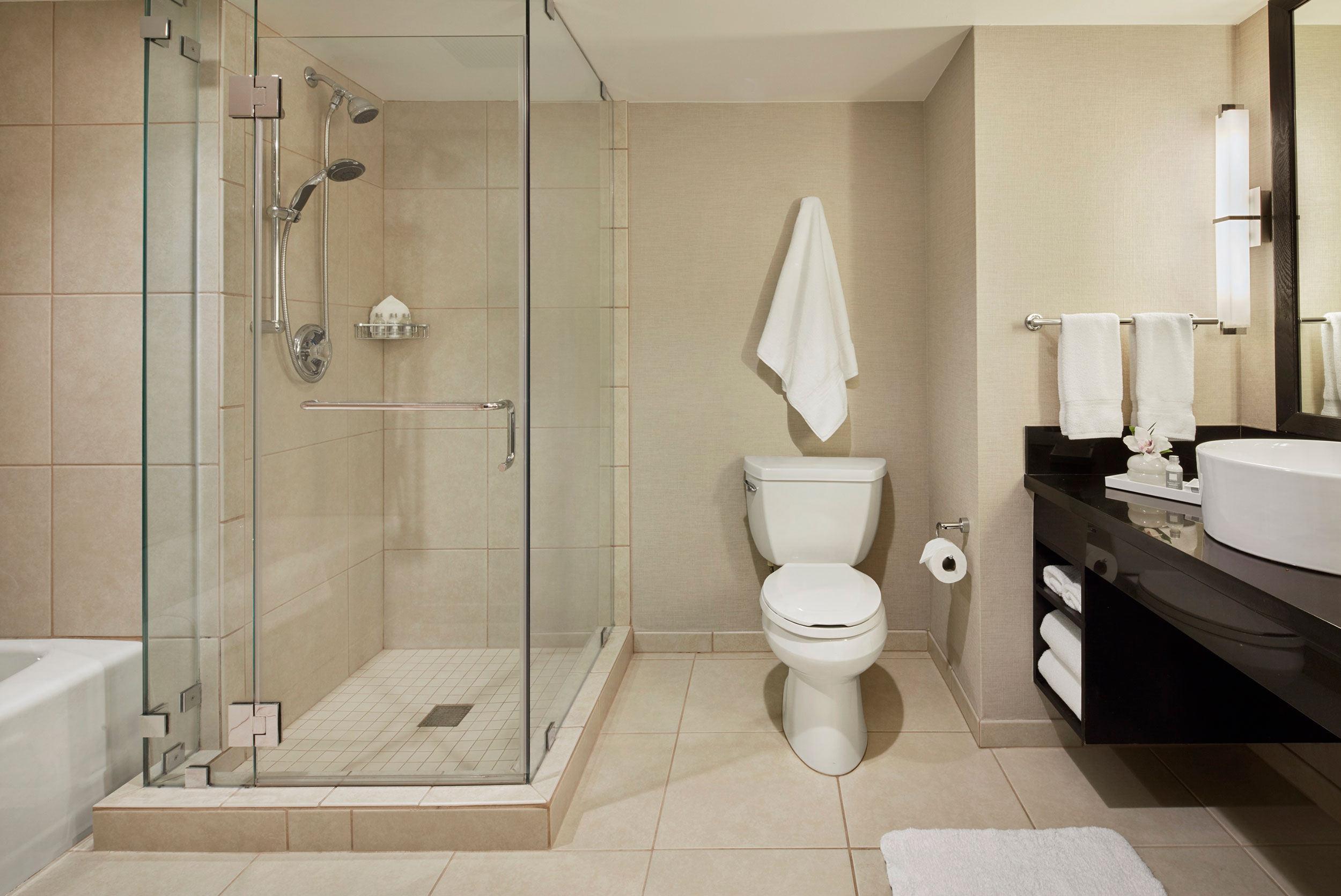 Deluxe hotel bathroom with a glass-enclosed shower, soaking tub, toilet, vessel sink, and neutral tile finishes.