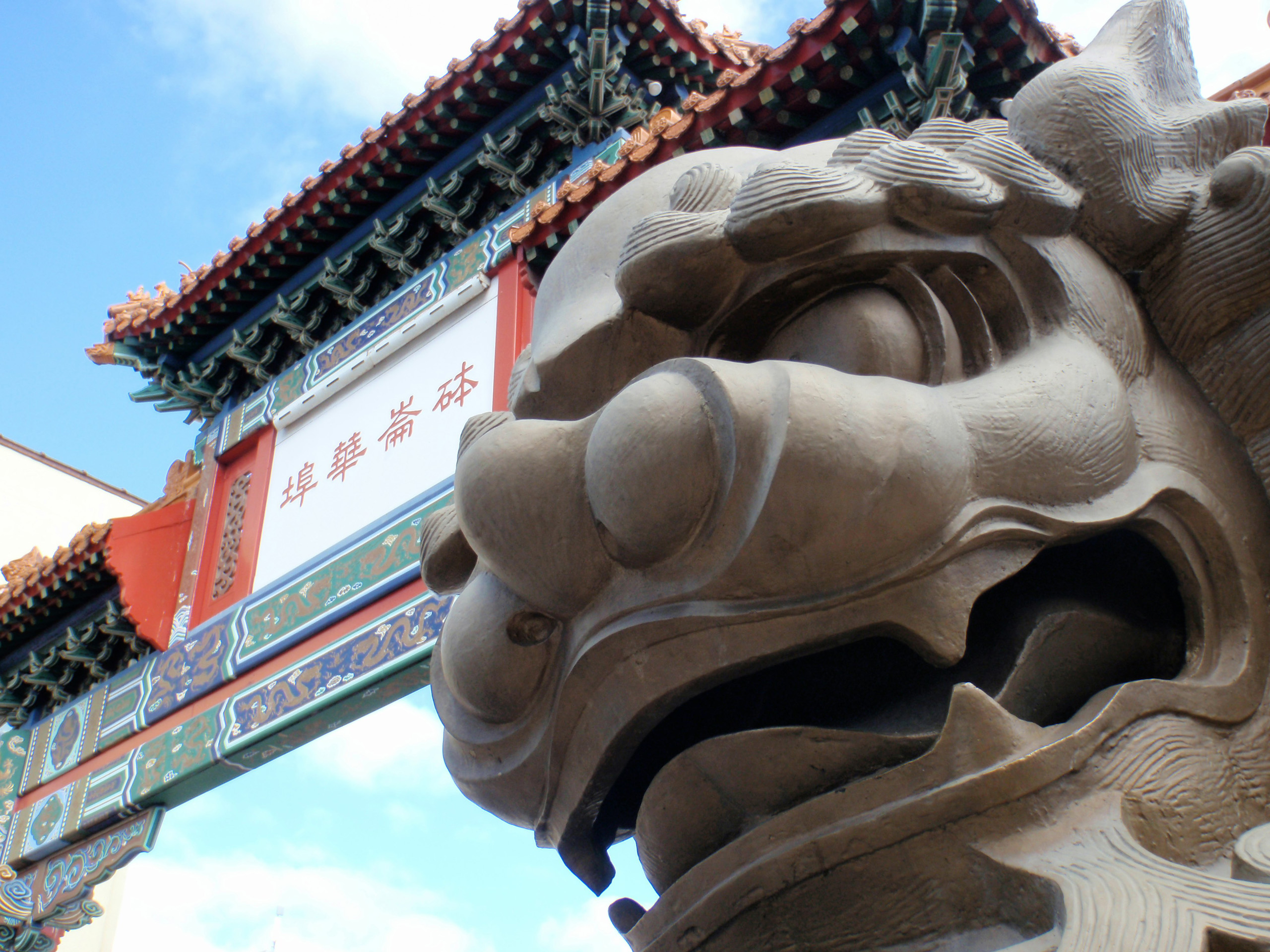 Stone guardian lion beside ornate Chinatown gateway.