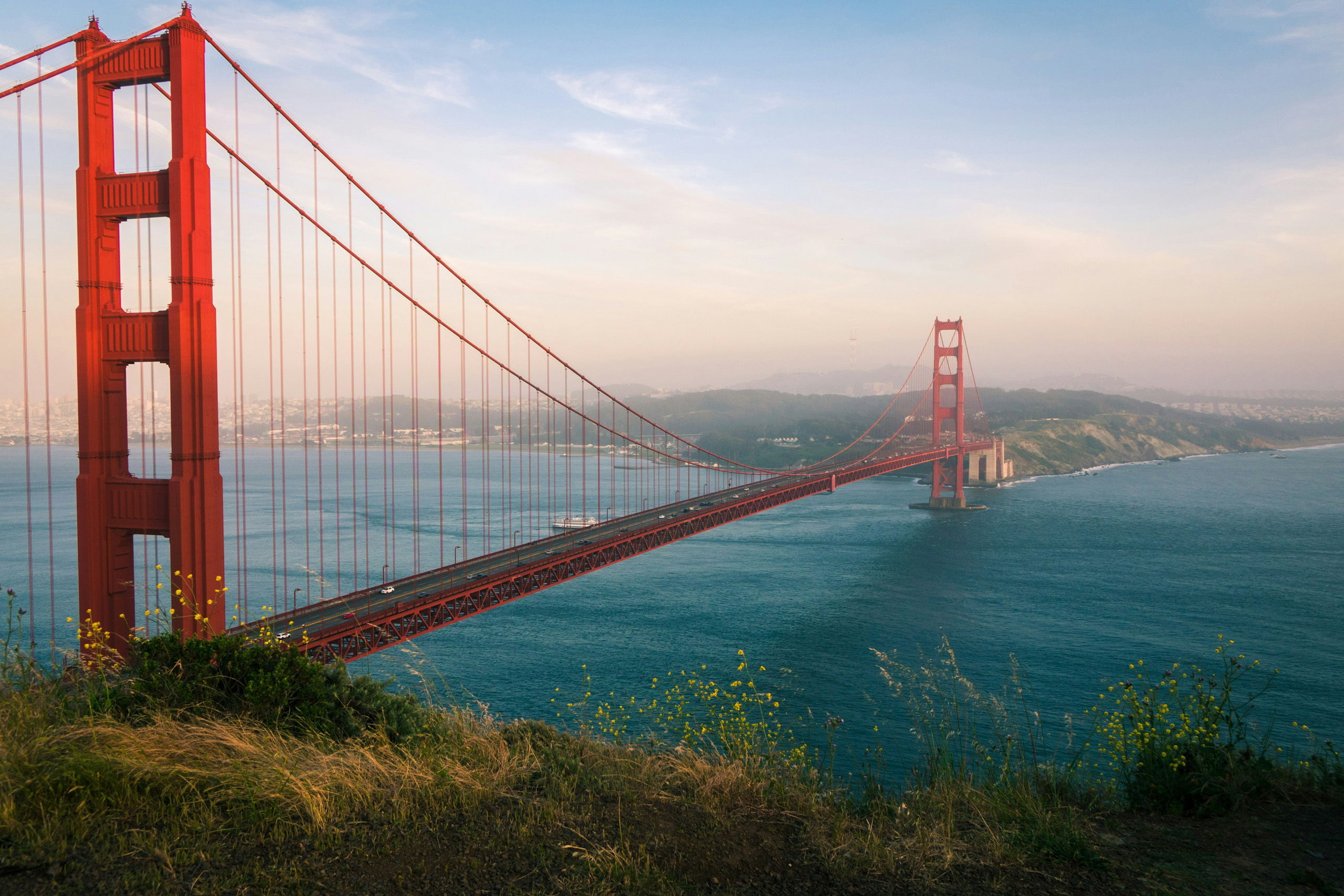 Golden Gate Bridge spanning blue water beneath hazy sky.