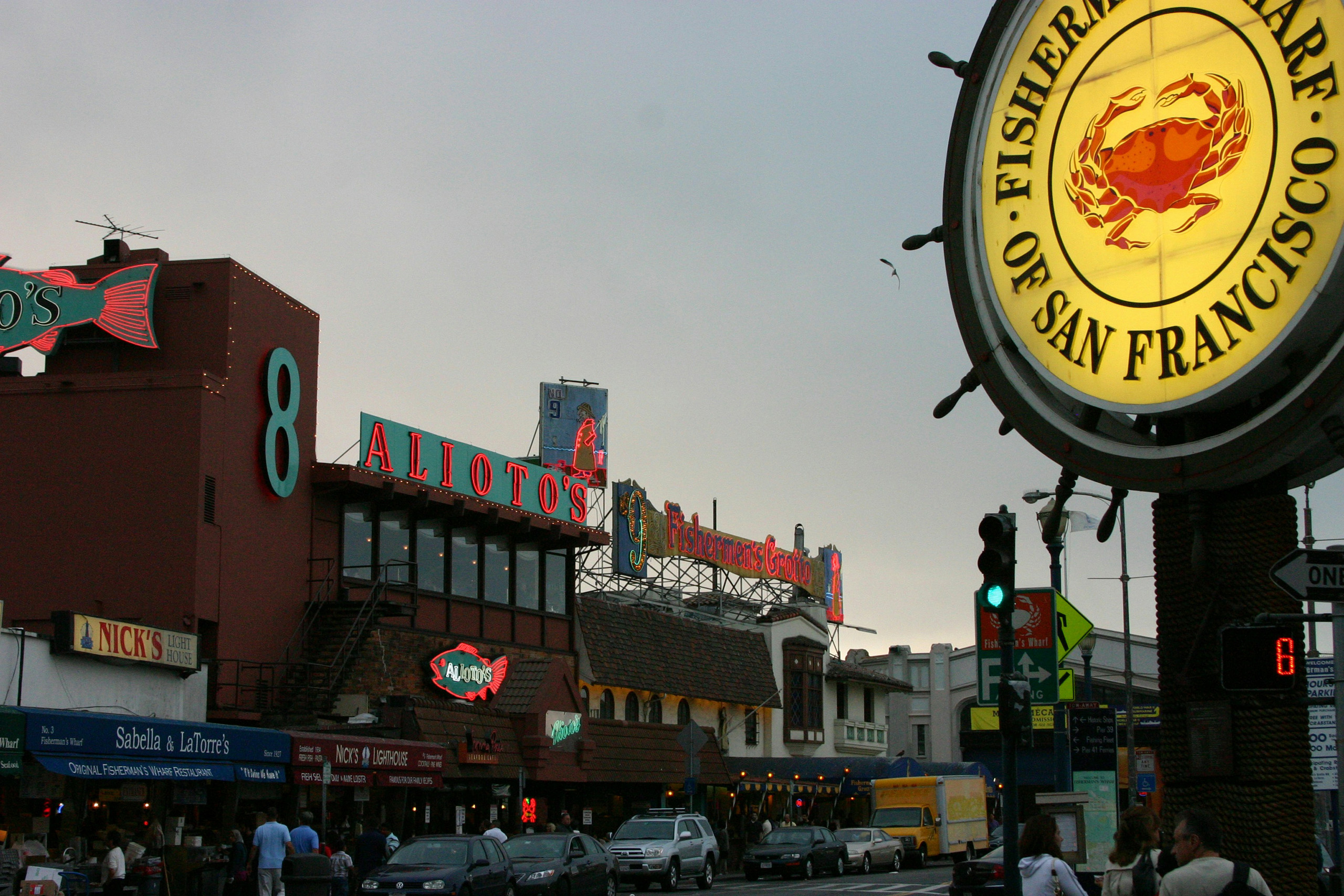Fisherman’s Wharf street with restaurants, signs, cars, and pedestrians.