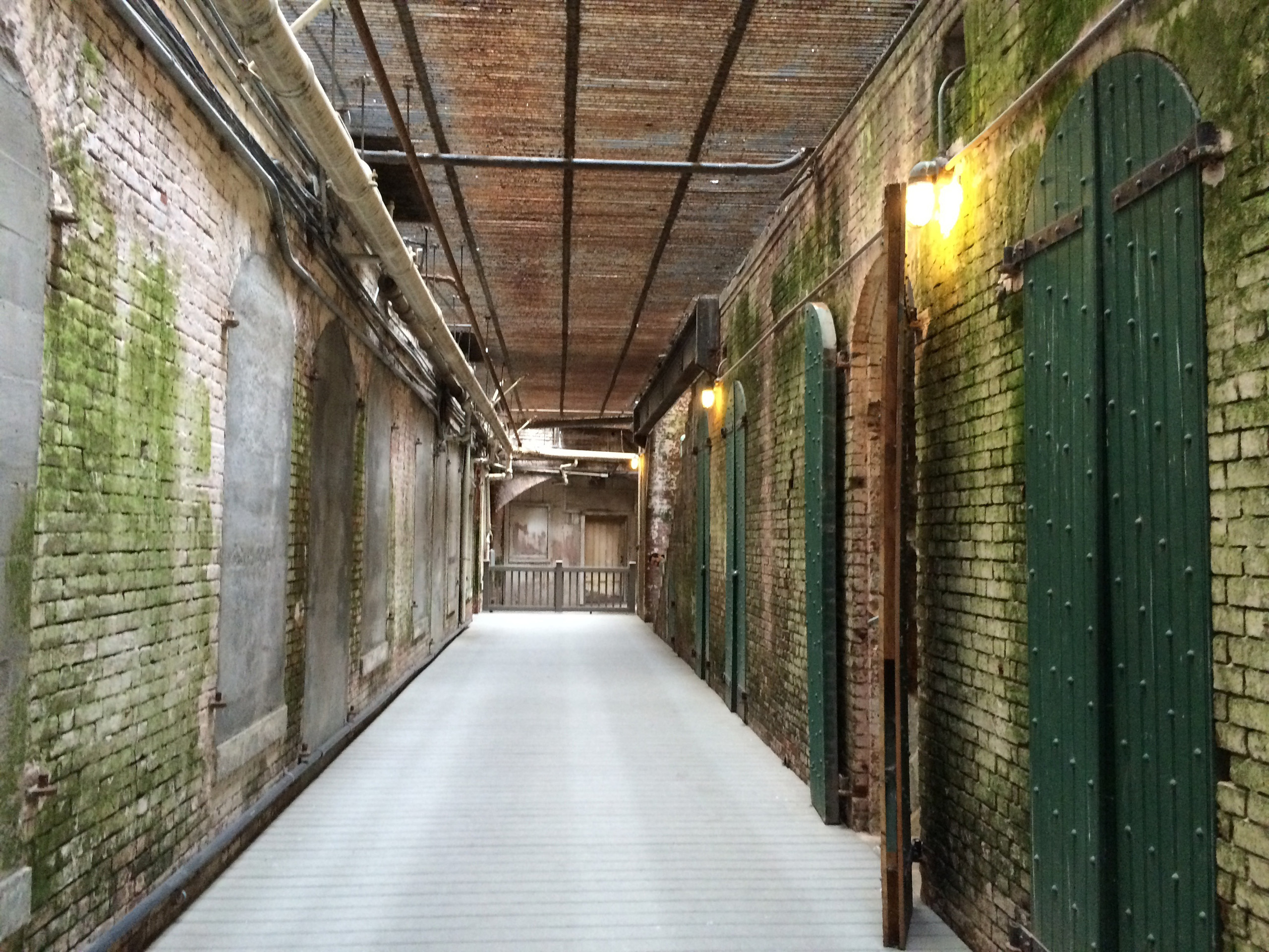 Alcatraz corridor with brick walls and green cell doors.