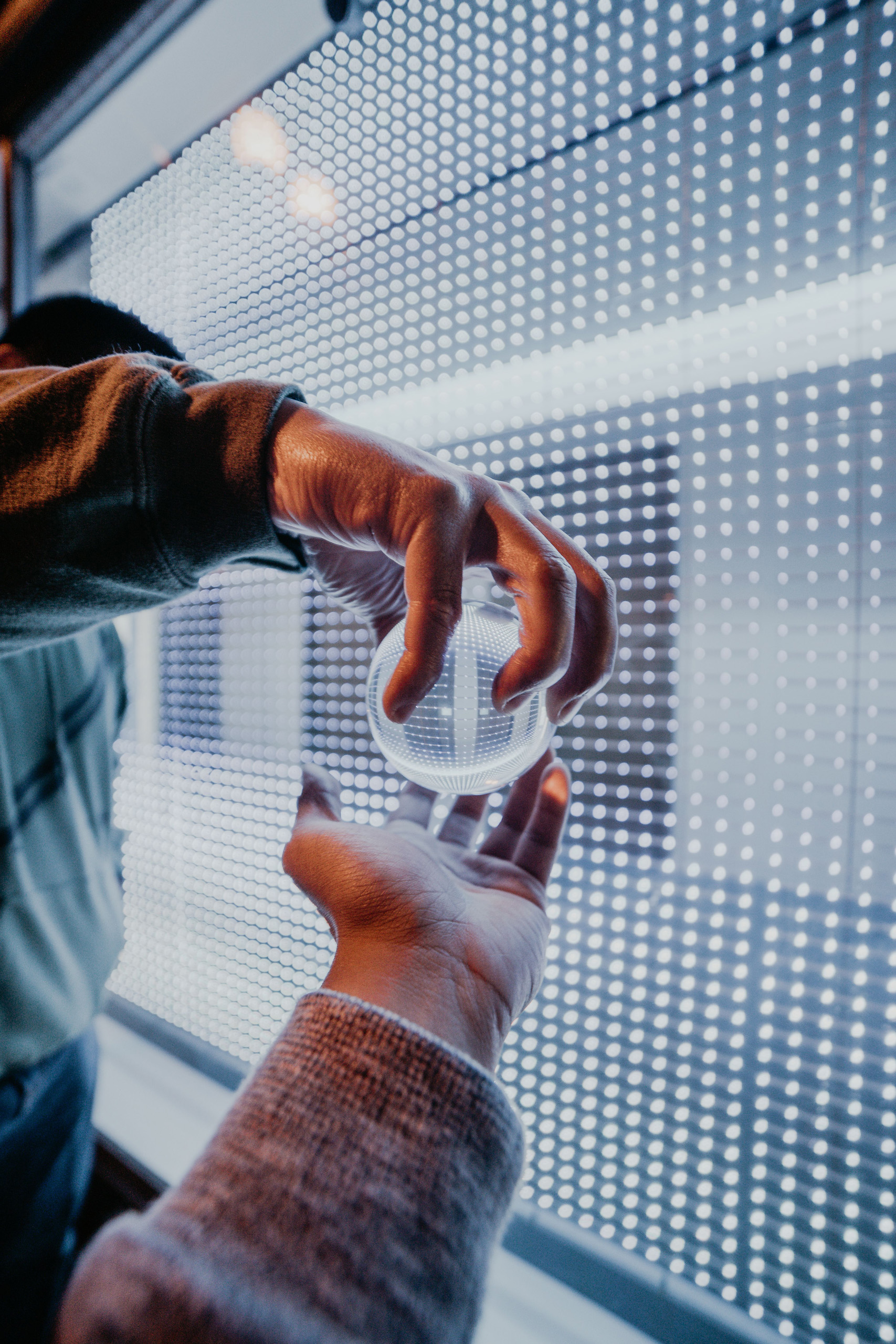 Hands holding a clear glass sphere in front of an illuminated display.