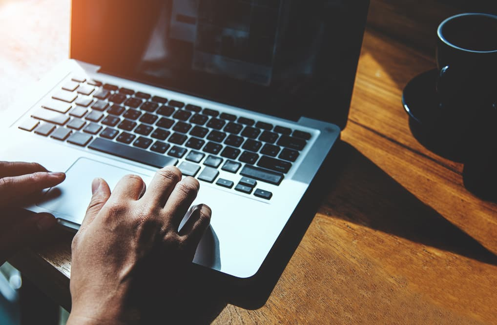 Hands typing on a laptop next to a cup of coffee