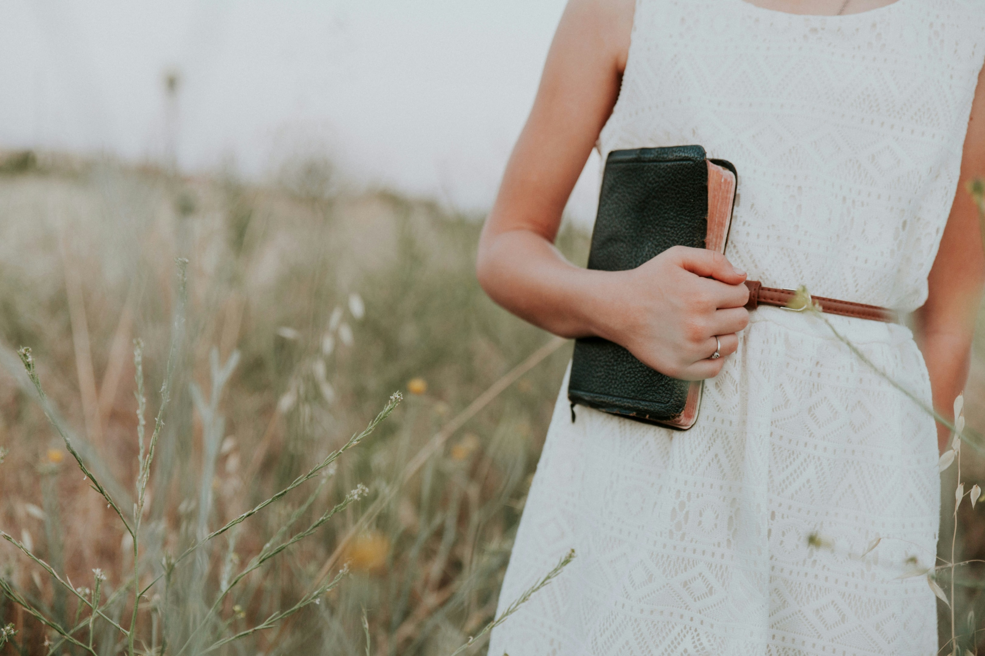 A photo of a young woman in a white dress holding a Bible and standing in a field.