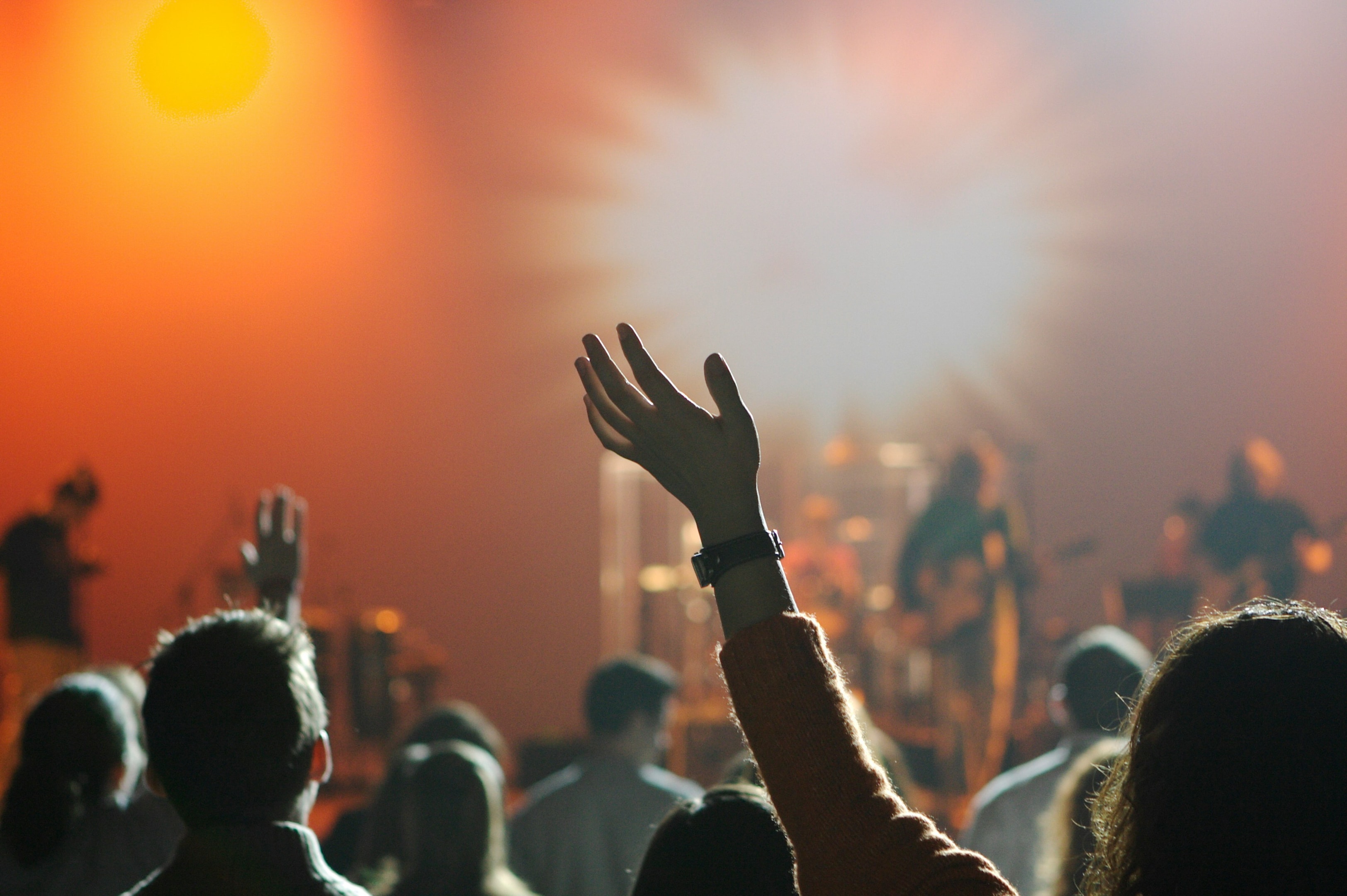 A photo of a worship service at a Christian church. A woman's hand is raised in the air, and there is a band playing.