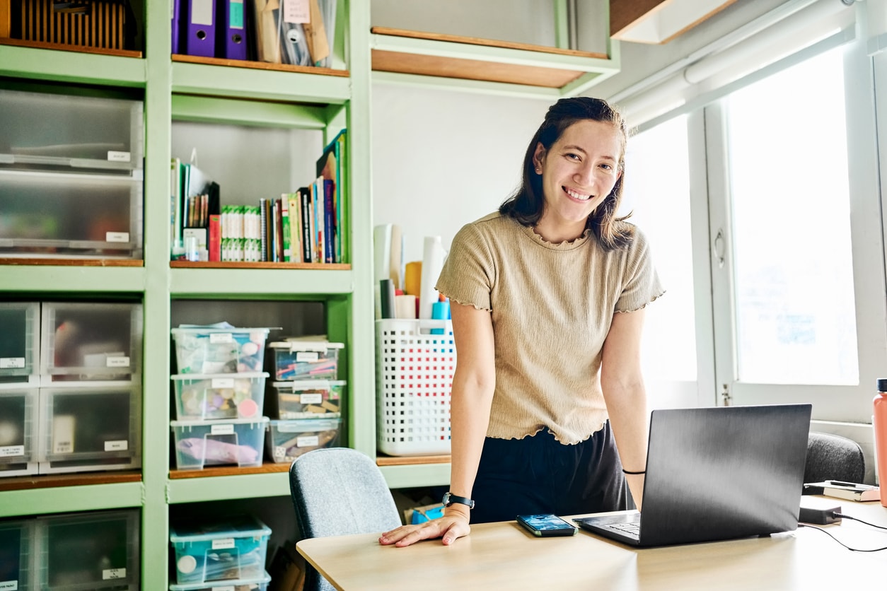 A photo of a smiling young woman at a desk behind a computer with office supplies.
