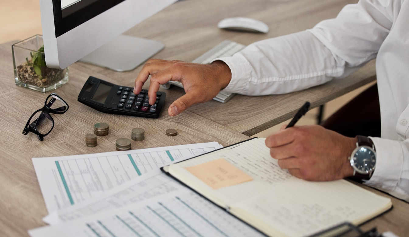 A photo of a man using a calculator and taking notes on a sheet of paper.