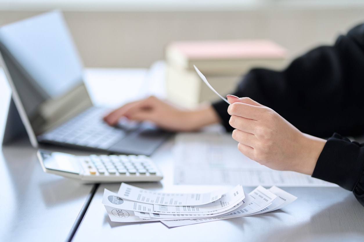 A photo of a woman keeping track of receipts with expense management software and a calculator.
