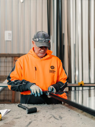 Worker in hi-vis assembling a double glazed window unit at a workshop bench