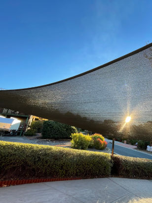 Large curved shade sail stretched over a driveway and garden against a clear blue sky