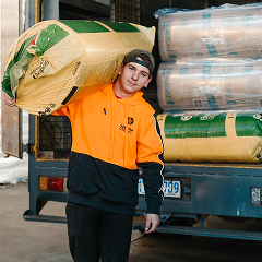 Worker in hi-vis carrying a bagged pack of insulation batts on his shoulder beside a loaded truck