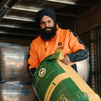 Worker in a hi-vis Just Rite jacket lifting a bagged pack of insulation batts inside a delivery truck