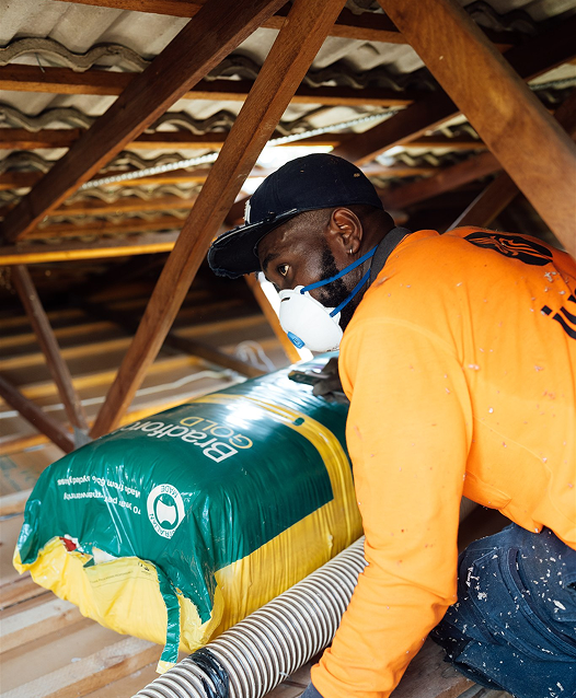Installer in a dust mask moving a pack of Bradford Gold insulation batts through a roof cavity