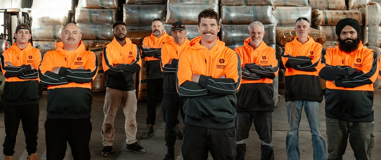 Team of installers in orange hi-vis uniforms standing with arms folded in an insulation warehouse