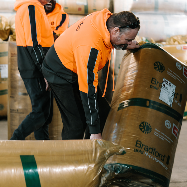 Workers in hi-vis handling compressed bales of Bradford Gold insulation in a warehouse