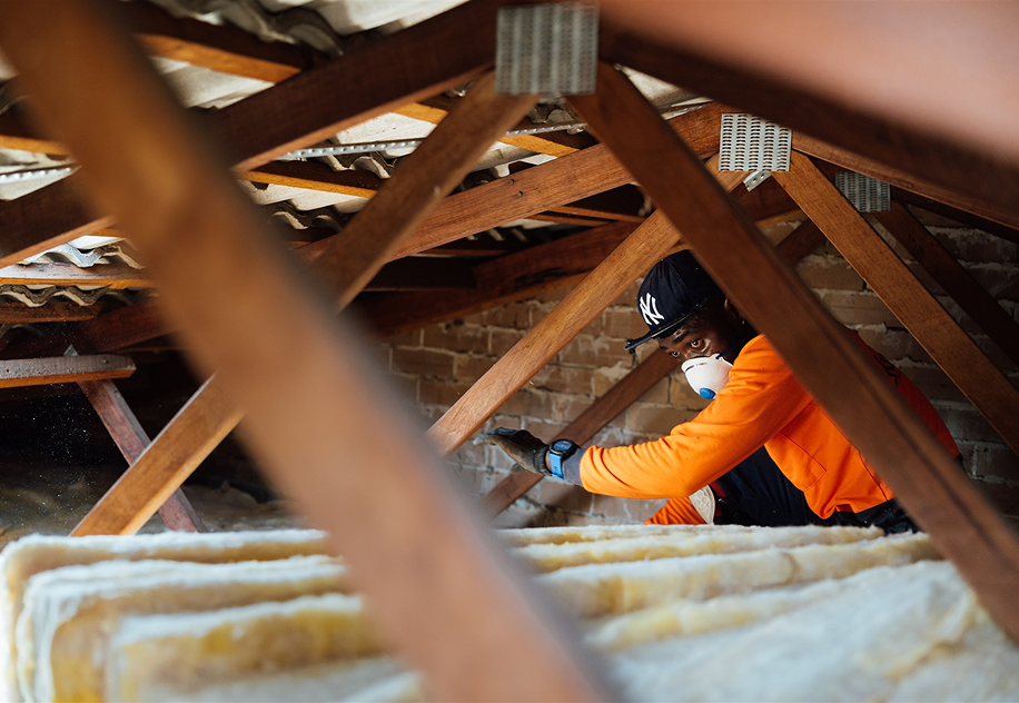 Installer in a dust mask laying insulation batts in a roof cavity between timber trusses